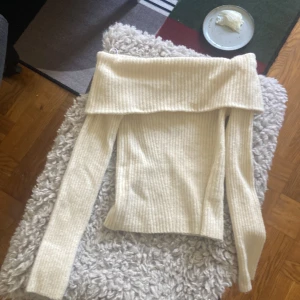 Beige ribbad offshoulder tröja - Säljer en stilren beige ribbad tröja med offshoulder-design. Perfekt för en trendig look med långa ärmar och mjukt material. Passar bra till både jeans och kjol. 