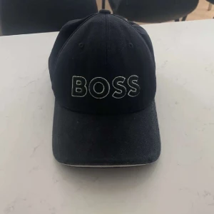 Svart keps från Boss - Snygg svart keps från Boss med broderad logga framtill. Justerbar rem baktill för perfekt passform. Perfekt för en stilren look.