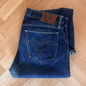  RRL selvedge jeans Limited edition 1-200 - Snygga mörkblå jeans från RRL med knappgylf och klassisk femficksdesign. Jeansen har en stilren broderad detalj på bakfickan och en läderpatch med logotyp baktill. Perfekta för en avslappnad stil. Helt nya selvedge jeans, gjorda i en limited edition upplaga. 1-200 st i hela världen 
