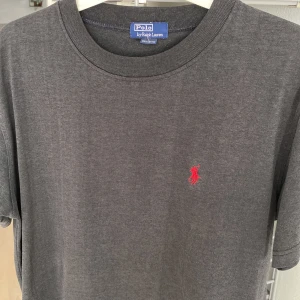 Ralph Lauren T-shirt  - Säljer en stilren t-shirt från Ralph Lauren med det klassiska röda broderade logotypen på bröstet. Tillverkad i 100% bomull för en bekväm passform. Perfekt för en avslappnad look.