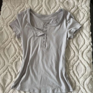 Grå kortärmad topp från Shein - Säljer en grå topp från Shein i storlek XS. Toppen är kortärmad med knappar framtill och har en tight passform. Materialet är mjukt och skönt mot din hud. Andvänt kanske 1-2 gånger.