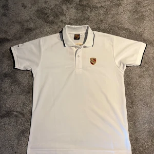 Vit pikétröja från Porsche - Säljer en stilren vit pikétröja från Porsche med broderad logotyp på bröstet och ryggen. Tröjan har korta ärmar och en klassisk krage med knappar. Helt ny! Sitter lite mer som S men passar både! Skriv vid funderingar!