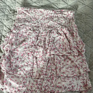 Blommig kjol från BikBok - Söt blommig kjol från BikBok i storlek XS. Kjolen har ett elastiskt midjeband och flera lager volanger som ger en lekfull look. Perfekt för varma dagar med sitt lätta och luftiga material.
