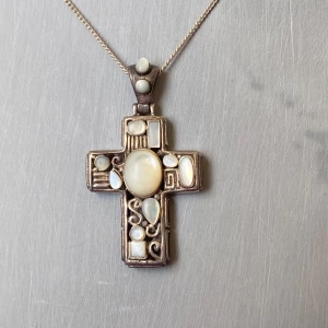 Silverhalsband med korshänge - Elegant silverhalsband med ett korsformat hänge dekorerat med vita stenar . Hänget har en unik design med olika former av pärlor infattade i ett intrikat mönster. Kedjan är tunn och smidig med en enkel låsning.