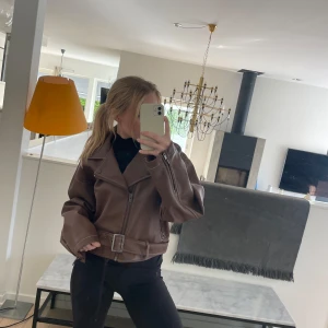 Brun skinnjacka med bälte - Snygg brun skinnjacka med dragkedja och bälte i midjan. Jackan har en cool oversized passform och långa ärmar. Perfekt för en trendig look!