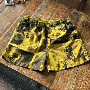 Gula basketshorts med Michael Jordan-tryck - Snygga gula shorts med svart tryck av Michael Jordan och basketmotiv. De har elastisk midja med snörning och coola grafiska detaljer över hela tyget. Perfekta för dig som gillar sportig streetstyle och vill sticka ut med ett unikt plagg.