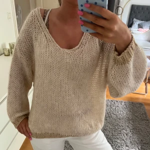 Beige stickad tröja med v-ringning - Säljer en beige stickad tröja med v-ringad hals och ribbade muddar i guld!! Tröjan har långa ärmar och är gjord i ett luftigt, grovstickat material som känns både chill och trendigt. Står ingen storlek i!