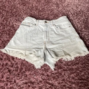 Vita högmidjade jeansshorts med fransar - Snygga vita jeansshorts med hög midja och råa fransade kanter. Klassisk femficksmodell med knapp och dragkedja framtill. Perfekta för sommaren och ger en chill vibe till din outfit. Finns likadana i grå.