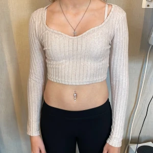 Beige ribbad croppad topp från SHEIN - Säljer en beige croppad topp från SHEIN i storlek XS. Toppen har långa ärmar, ribbat tyg och en snygg v-ringad urringning. Perfekt att matcha med höga jeans eller kjol för en trendig look.