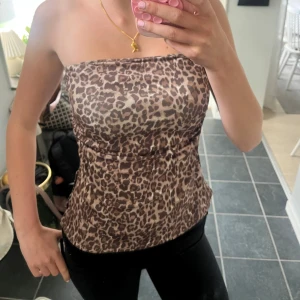 Leopardmönstrad tubtopp i satinlook - Snygg tubtopp med leopardmönster i bruna och beige toner. Toppens material har en lätt glansig satinlook och är figurnära med en liten slits på sidan. Perfekt för dig som vill sticka ut med ett djurmönster och gillar trendiga detaljer.