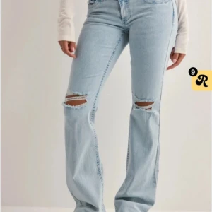 Ljusblå bootcut jeans med slitningar - Snygga ljusblå jeans med bootcut passform och slitna hål på båda knäna. Jeansen har klassisk femficksdesign och är tillverkade i jeansmaterial. Perfekta för en avslappnad och trendig look.