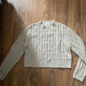 Beige stickad tröja från Zara - Säljer en beige stickad tröja från Zara med snyggt hålmönster och ribbad hals. Tröjan är lite croppad och har långa ärmar, perfekt för lager-på-lager-stil. Enkel att matcha med både jeans och kjol.