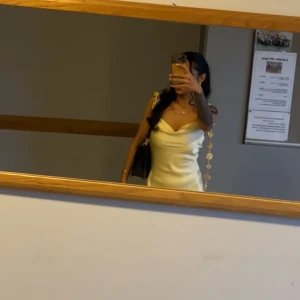 Ljusgul satinklänning med smala axelband - Supersöt ljusgul klänning i satin med smala axelband och snygg draperad urringning. Klänningen är kort och har en elegant, figurnära passform som ger en chic vibe. Perfekt för dig som vill sticka ut med en stilren och trendig look. Använd endast en gång 