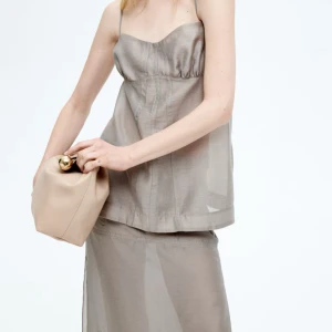 Beige linnetopp med tunna axelband - Säljer en stilren beige linnetopp med tunna axelband och lätt glansig finish. Toppen har en söt byst med rynk och sömdetaljer framtill som ger en snygg siluett. Perfekt för varma dagar och enkel att matcha med både kjol och jeans. Aldrig använd❤️🫶