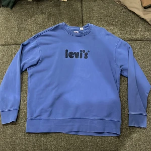 Blå sweatshirt från Levi's i relaxed fit - Säljer en blå sweatshirt från Levi's i relaxed fit med broderad logga på bröstet. Tröjan har rund halsringning, långa ärmar och är gjord i mjuk bomull. Perfekt för dig som gillar en chill och stilren look.