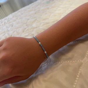 Blått pärlarmband med vita detaljer - Sött armband med små blå pärlor och några vita pärlor som accent. Tunt och minimalistiskt, perfekt för att ge en färgklick till din outfit. Passar dig som gillar enkel och stilren design.
