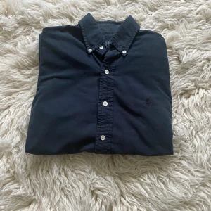 Mörkblå/svart Ralph lauren skjorta xs - Klassisk mörkblå/svart skjorta från Polo Ralph Lauren i bomull. Skjortan har button down-krage, vita knappar och lång ärm. Broderad logga på bröstet i svart för en clean look.                                                            Skickar nästan alltid inom 1-2 dagar🚚.                            Tröjan är xs men passar också om man är s och vill att den sitter tight.