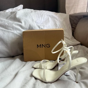 Helt nya med pris lapp  - Stilrena vita sandaler från MNG med smala remmar och knyt runt vristen. Skorna har fyrkantig tå och hög klack, perfekta för att lyfta din outfit. Köptes för 500 säljer för 350 helt nya 