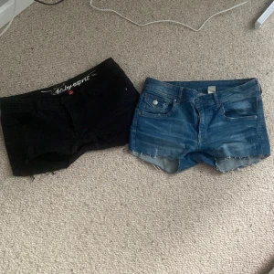 Två par jeansshorts, svart & blå lågmidjade  - Säljer två par snygga shorts: ett par svarta från dc by esprit med råa kanter och ett par klassiska blå jeansshorts med slitna detaljer. Båda har femficksmodell, dragkedja och bälteshällor. Perfekta för varma dagar och chill stil.