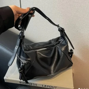 Svart axelväska  - Snygg svart axelväska i skinnimitation med justerbart axelband och dragkedja upptill. Väskan har en stilren design, silverfärgade detaljer och extra fack med dragkedja på sidan. Perfekt storlek för mobil, plånbok och andra essentials.