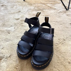 Svarta Dr. Martens sandaler i skinn - Chunky svarta sandaler från Dr. Martens med breda remmar i skinn, justerbart spänne vid ankeln och klassisk gul söm runt sulan. Använt en gång.