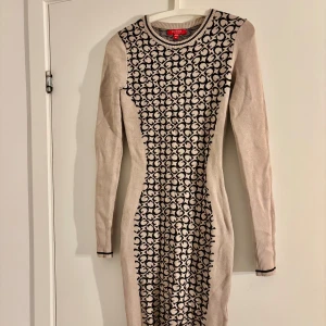 Beige och svart stickad klänning Guess XS - Supersnygg beige stickad klänning från Guess i figurnära modell med svarta mönsterdetaljer framtill. Långärmad och med rund halsringning. Perfekt för dig som gillar stilrena men ändå unika plagg. Kommer med Guess dustbag. Perfekt nu inför hösten!