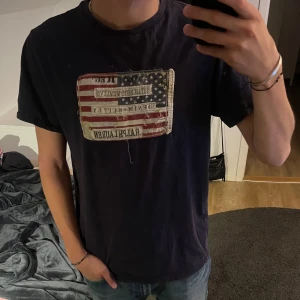 Denim and supply T-shirt  - Snygg mörkblå t-shirt från Ralph Lauren Denim & Supply med amerikansk flagga och broderad logga på bröstet. Klassisk passform, rund hals och korta ärmar. Tillverkad i mjuk bomull, perfekt till jeans eller shorts. Lite lösa trådar men annars väldigt bra skick.