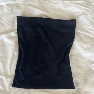 Svart tubtopp från H&M XS - En enkel och stilren svart tubtopp från H&M i storlek XS. Toppen är axelbandslös och har en klassisk bandeau-form som sitter tight mot kroppen. Perfekt att matcha med jeans eller kjol för en clean look.