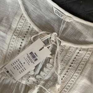 Vit boho-klänning från ONLY - Superfin vit klänning från ONLY med snygga virkade detaljer och snörning framtill. Lätt och luftig med en avslappnad passform. Perfekt för sommarens alla tillfällen, enkel att styla med sandaler eller sneakers. Stär ej för postens slarv Köpt är köpt, gär ej att returneras. Pris gär att diskuteras