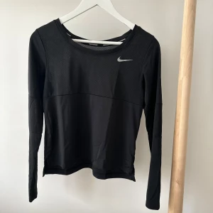 Nike svart långärmad Dri-FIT träningströja - Svart långärmad träningströja från Nike med Dri-FIT-teknologi. Tröjan har meshpaneler upptill och på ärmarna för extra ventilation, rund halsringning och en liten Nike-logga på bröstet. Perfekt för löpning eller gym.