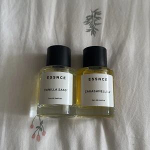 ESSNCE Vanilla Sass' & Carashmellow - Två stilrena parfymflaskor från ESSNCE: Vanilla Sass' och Carashmellow. Flaskorna är runda i genomskinligt glas med svarta matta korkar och vita etiketter med minimalistisk text. Innehållet är ljusgult och ger en fräsch och modern känsla.