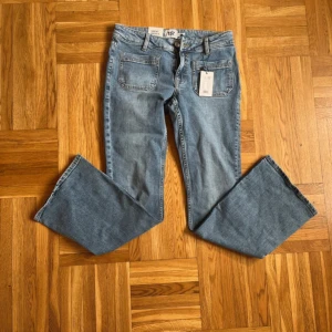 Blå bootcut jeans från Gina Tricot - Snygga blå jeans från Gina Tricot med bootcut-ben och klassisk femficksdesign. Jeansen har en ljus tvätt och normal passform, perfekta för en trendig vardagslook. Stängs med dragkedja och knapp framtill.