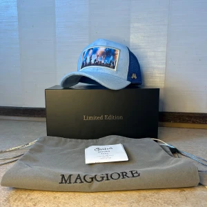 Blå limited edition keps Maggiore ABBA - Exklusiv blå keps från Maggiore med mesh på sidorna och ett färgstarkt motiv framtill som visar en konsertscen på ABBA. Kepsen har böjd skärm och metallogo på sidan. Kommer med originalpåse och box. Perfekt för dig som vill sticka ut med en unik accessoar.