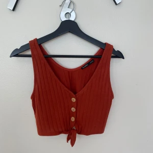 Rostfärgad ribbad linnetopp Pull&Bear - Superfin croppad linnetopp från Pull&Bear i en varm rostbrun färg. Toppen har ribbad struktur, v-ringning, knappar framtill och en snygg knytning nedtill. Använd fåtal gånger.