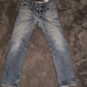 Blå jeans från Armani Jeans, strl 32/31 - Snygga blå jeans från Armani Jeans i klassisk tvätt med lätt slitning. Modellen har raka ben, fem fickor och läderpatch med logga bak. Båda fram fickorna har hål därav priset.