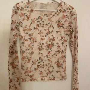 Blommig mesh topp från Stradivarius - Supersöt långärmad mesh topp från Stradivarius med blommigt mönster. Tunn och lätt genomskinlig med rund halsringning, perfekt att styla med jeans eller kjol. Den har en bra passform och passar även en storlek S och xs