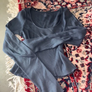 Mörkblå ribbad långärmad topp - Snygg mörkblå långärmad topp med ribbad struktur och rundad, djup urringning. Modellen är figurnära och något croppad. Säljer denna pga av att jag inte är så förtjust i croppade tröjor. Tröjan är köpt på Brandy Melville 