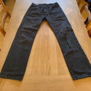 Svarta Levi's 501 jeans W30 L30 - Klassiska svarta Levi's 501 jeans med raka ben och normal passform. Jeansen har fem fickor, knappgylf och den ikoniska läderpatchen bak i midjan. 