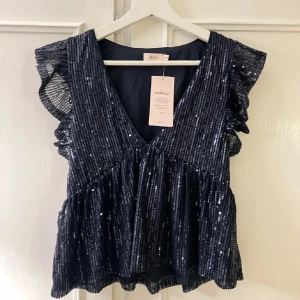 Glittrig mörkblå topp från Nelly - Topp från Nelly med glittriga paljetter, v-ringning och volangiga ärmlösa axlar. Köpte helt ny på plick andvänd ändas EN gång! jätte bra sick skriv för fler bilder rätt i storlek!💞sitter som xxs och xs!