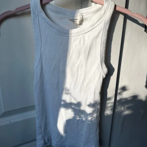 Vit ribbad linnetopp från Gina Tricot - Säljer en klassisk vit ribbad linnetopp från Gina Tricot, kollektionen Basically Basics. Perfekt att styla till jeans eller kjol. Tidlös modell med rund halsringning och ärmlös design.