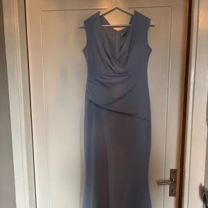 Ljusblå långklänning från Goddiva London - Säljer en elegant ljusblå långklänning från Goddiva London. Klänningen har en draperad v-ringning och är ärmlös med figurnära passform. Perfekt för bal eller festliga tillfällen. Materialet känns mjukt och följsamt.