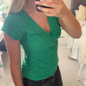 Grön v-ringad blus med struktur - Säljer en grön blus med v-ringning och korta ärmar. Toppen har en snygg rynkdetalj framtill och är tillverkad i ett strukturerat material. Från Dobber i storlek s