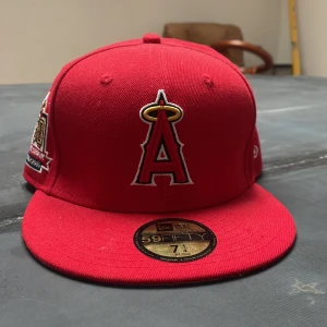 Röd keps från New Era 59FIFTY Los Angeles Angels - Röd fitted keps från New Era 59FIFTY med Los Angeles Angels-logga framtill och 50-årsjubileumsmärke på sidan. 