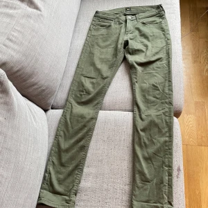 Olivgröna byxor från Lee - Säljer ett par olivgröna byxor från Lee med klassisk femficksdesign och raka ben. Byxorna har knapp och dragkedja framtill samt Lee-logga på bakfickan. Perfekta för en avslappnad stil.