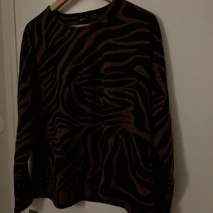Brun och svart zebramönstrad tröja - Säljer en stickad tröja med zebramönster i brunt och svart. Tröjan har rund halsringning och långa ärmar. 