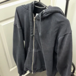 Svart hoodie ZARA - En klassisk svart hoodie med dragkedja och huva. Tröjan har långa ärmar, fickor framtill och justerbara snören i huvan. Perfekt för en avslappnad stil.