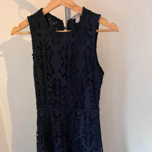 Marinblå spetsklänning från H&M - Säljer en marinblå ärmlös klänning från H&M med vackra spetsdetaljer och blommigt mönster. Klänningen har rund halsringning och är fodrad undertill. Perfekt för dig som gillar en klassisk och stilren look.