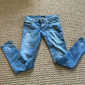 Blå jeansbyxor från Tiger of Sweden - Säljer ett par klassiska blå jeans från Tiger of Sweden i modellen Slender. Byxorna har fem fickor, dragkedja och knapp framtill samt raka ben. Perfekta för dig som gillar stilrena och tidlösa jeans.