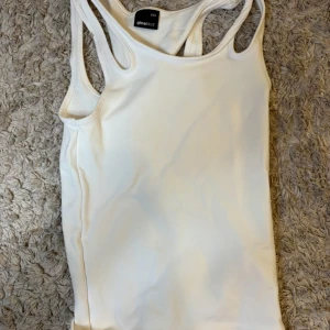 Vit linnetopp från Gina Tricot - Säljer en klassisk vit linnetopp från Gina Tricot. Toppen har en enkel och stilren design med brottarrygg och är tillverkad i ett mjukt och stretchigt material. Perfekt att matcha med jeans eller kjol.