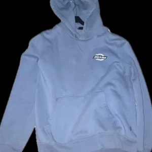 Ljusblå hoodie från Dickies - Säljer en ljusblå hoodie från Dickies med stor logga på ryggen och mindre logga på bröstet. Tröjan har huva och en stor magficka framtill. 